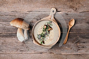 Wooden bowl of cream mushroom soup with fried mushrooms, vegetables, spices, raw boletus edulis mushroom on wooden