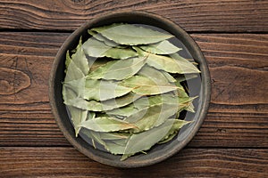 Wooden bowl of dried laurel leaves. Green bay leaves on wooden board.