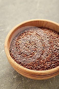 Wooden bowl with flax seeds on grey background. Vertical photo