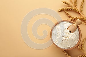 Wooden bowl with flour and spikelets of wheat. Wheat flour on beige background. Top view