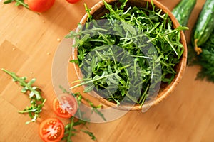 Wooden bowl of fresh green, natural arugula with cherry tomatoes and cucumbers