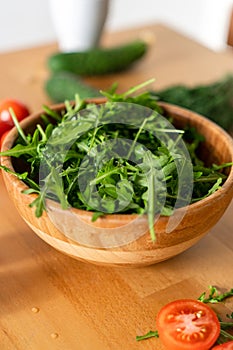 Wooden Bowl of fresh green, natural arugula with red tomatoes on a wooden background