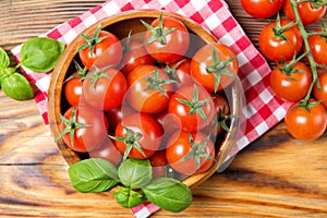 Wooden bowl with fresh ripe cherry tomatoes and basil leaves on a wooden table with red checkered towel, healthy food, top view