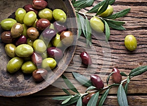 Wooden bowl full of olives and olive twigs.