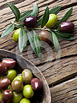 Wooden bowl full of olives and olive twigs.