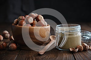 Bowl of hazelnuts, glass jar of raw organic hazelnut butter or paste on kitchen table photo