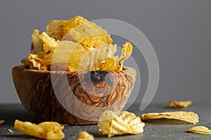 A wooden bowl of kettle cooked potato chips with crunchy ruffled texture.
