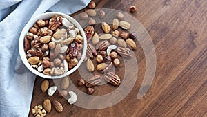 Wooden bowl with mixed nuts on table top view. Healthy food and snack. Walnut, pistachios, almonds, hazelnuts and