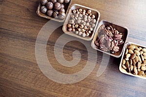 Wooden bowl with mixed nuts on table top view. Healthy food and snack. Walnut, pistachios, almonds, hazelnuts and