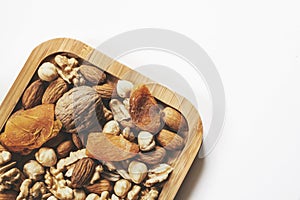 Wooden bowl with mixed nuts on white table top view. Healthy food and snack. Walnut, pistachios, almonds, hazelnuts