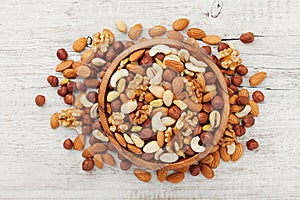 Wooden bowl with mixed nuts on white table top view. Healthy food and snack. Walnut, pistachios, almonds, hazelnuts and cashews.