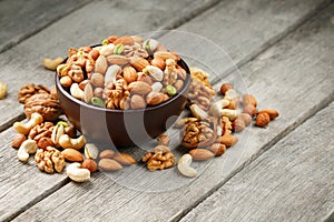 Wooden bowl with mixed nuts on a wooden gray background. Walnut, pistachios, almonds, hazelnuts and cashews, walnut