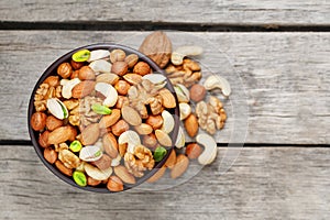 Wooden bowl with mixed nuts on a wooden gray background. Walnut, pistachios, almonds, hazelnuts and cashews, walnut