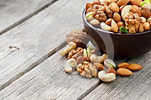 Wooden bowl with mixed nuts on a wooden gray background. Walnut, pistachios, almonds, hazelnuts and cashews, walnut