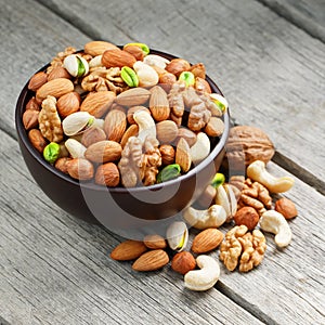 Wooden bowl with mixed nuts on a wooden gray background. Walnut, pistachios, almonds, hazelnuts and cashews, walnut