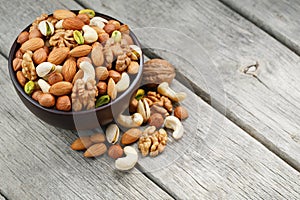 Wooden bowl with mixed nuts on a wooden gray background. Walnut, pistachios, almonds, hazelnuts and cashews, walnut