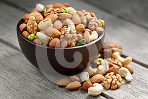 Wooden bowl with mixed nuts on a wooden gray background. Walnut, pistachios, almonds, hazelnuts and cashews, walnut