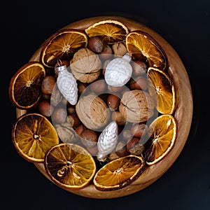 Wooden bowl with nuts, walnuts and hazelnuts. Dish decorated with Christmas baubles and slices of dried oranges