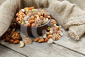 Wooden bowl with nuts on a wooden background, near a bag from burlap