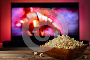 A wooden bowl of popcorn and remote control in the background the TV works. Evening cozy watching a movie or TV series