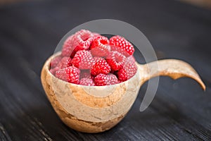 Wooden bowl with raspberries on black table