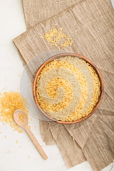 Wooden bowl with raw golden rice and wooden spoon on a white wooden background. Top view, close up