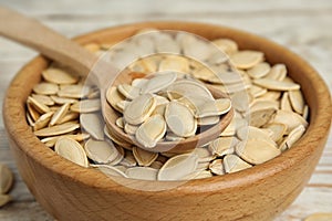 Wooden bowl and  of raw pumpkin seeds on white table, closeup