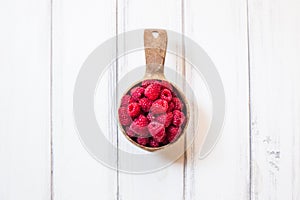 Wooden bowl with red raspberries on white table