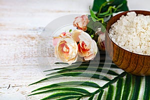 Wooden bowl with sea salt, rose and palm leaf