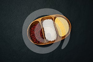 Wooden bowl with separate compartments filled with spices: red pepper, yellow corn grits and white coarse salt.