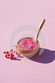 Wooden bowl with a spoon filled with pink bath sea salt.