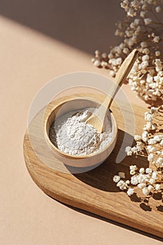 Wooden bowl with a spoon filled with white bath sea salt. Beauty treatment for spa and wellness on beige background.