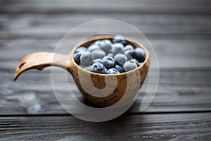 Wooden bowl with summer blueberries on black table. Macro