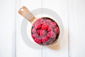 Wooden bowl with summer raspberries on white table