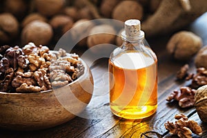 Wooden bowl of walnuts and bottle of essential nut oil on table.