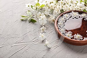 Wooden bowl with water and blooming flowers on grey textured background