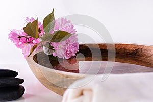 Wooden bowl with water and pink flower and black rock and towel isolated on white background