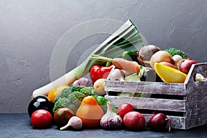 Wooden box with autumn harvest farm vegetables and root crops on dark kitchen table. Healthy and organic food.