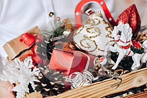 Wooden box with Christmas colorful different toys and decor in hands of a little girl