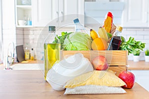 A wooden box of different food, fruit, vegetables, oil, water, sugar on the kitchen. Safe home delivery