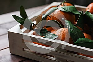 Wooden box of fresh tangerines with leaves on table