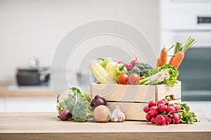 Wooden box full of fresh healthy vegetables. Broccoli carrot radish onion garlic corn on wooden kitchen table