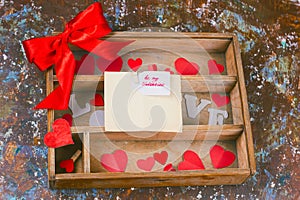 wooden box with paper hearts and present with red bow and lavel with be my valentine note