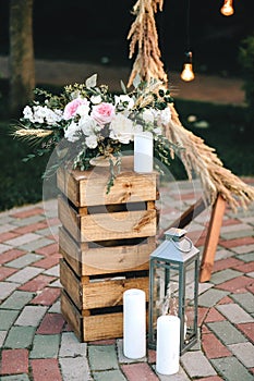 Wooden box pedestal bouquet of flowers and eucalyptus near the candlestick and white candles. Decor wedding arch in