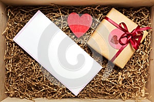 Wooden box with present wrapped in brown craft paper with red ribbon, with empty blank card