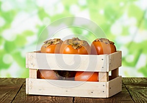 Wooden box with ripe sweet persimmons on dark table