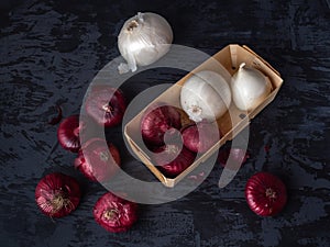 A wooden box with red and white onions lies on a dark background with a virgin.