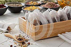 Wooden box of tea bags filled with dry medicinal herbs and flowers. Bowls of medicinal plants on background.