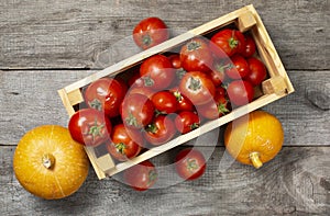 Wooden box with tomatoes and pumpkin on a wooden table background, rustic still life, harvest concept, products without