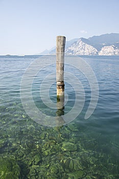 Wooden bricole for boats in the water, lake Lago Di Garda, morning light, mountains on the background
